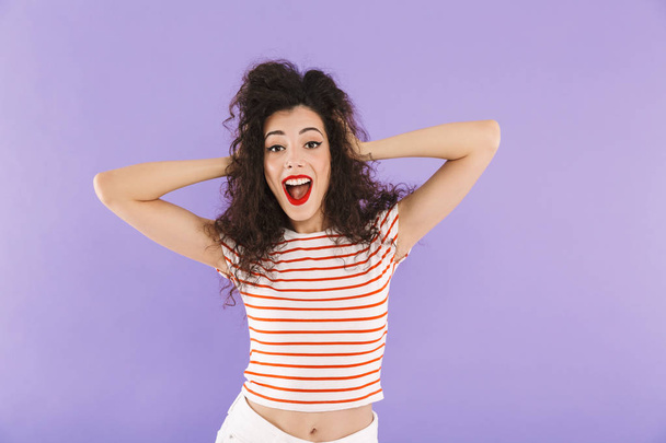 Image of glamour brunette woman with curly hair in summer wear laughing and looking at you isolated over violet background in studio - Foto, afbeelding