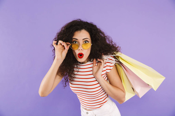 Portrait of an excited young casual woman carrying shopping bags isolated, showing peace gesture - Foto, imagen