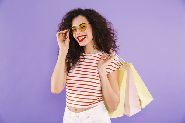 Portrait of a cheerful young casual woman carrying shopping bags isolated, showing peace gesture - Foto, Bild