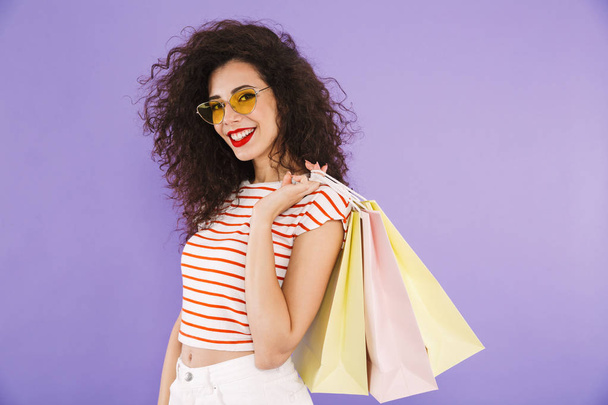 Portrait of a smiling young casual woman carrying shopping bags isolated, showing peace gesture - Фото, зображення