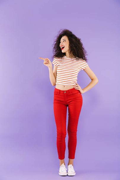 Full length portrait of a happy young casual woman posing while standing isolated, pointing away - Photo, image
