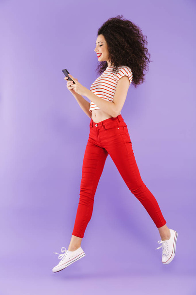 Full length portrait of a pretty young casual woman jumping isolated, using mobile phone - Foto, immagini