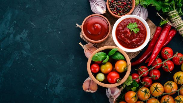 Ketchup sauce in a bowl. Cherry tomatoes, spices, chili peppers, olive oil, parsley. Top view. On a stone background. Free space for text. - Photo, Image