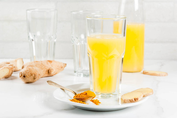 Indian cuisine recipes. Healthy food, detox water. Traditional Indian refreshing drink from turmeric and ginger, in glasses, bottles, on a white marble table. Copy space - Foto, immagini