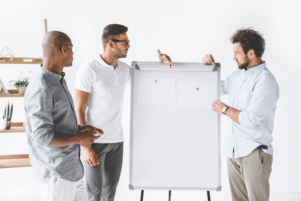 Мультикультурные бизнесмены обсуждают новую бизнес-стратегию на Белой доске в офисе
 - Фото, изображение