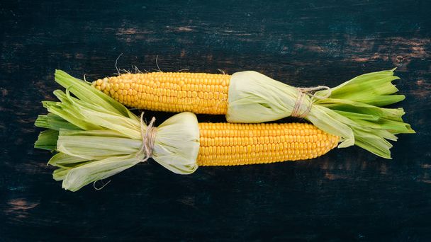 Fresh yellow corn on a black wooden table. Vegetables. Top view. Copy space. - 写真・画像
