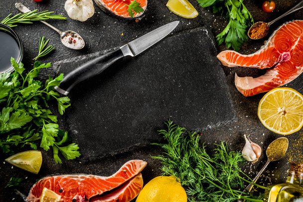 Ωμό ψάρι σολομός μπριζόλες με λεμόνι, βότανα, ελαιόλαδο, έτοιμη για τη σχάρα, πλάκα κοπής, σκούρο φόντο σκουριασμένο αντίγραφο χώρου - Φωτογραφία, εικόνα