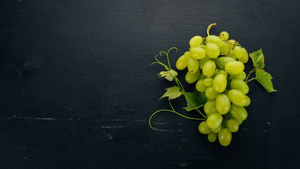 Fresh green grapes with leaves of grapes. Top view. On a black wooden background. Free space for text. - Fotoğraf, Görsel