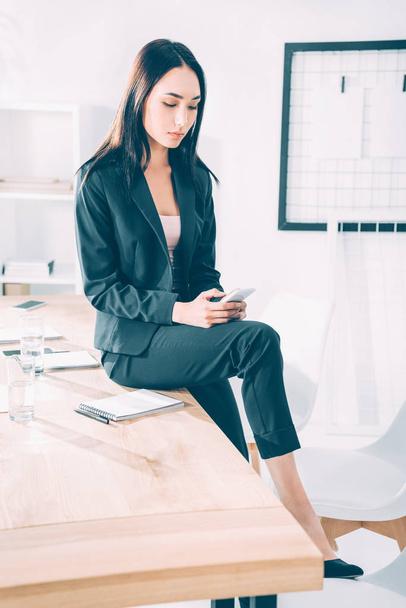 asiatique femme d'affaires en utilisant smartphone tandis que assis sur la table au bureau
 - Photo, image