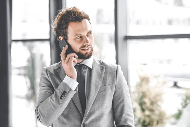portrait of businessman in suit talking on smartphone in office - Zdjęcie, obraz