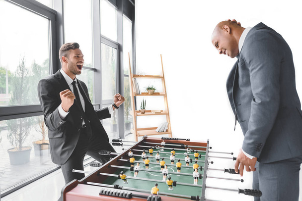 excited businessman playing table football with coworker in office - Fotó, kép