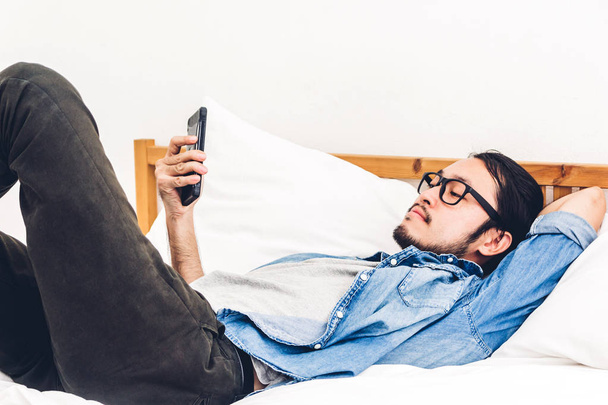 Человек расслабляется, используя и разговаривая со смартфоном на кровати дома.
 - Фото, изображение