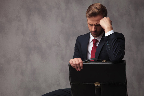 sad young businessman sitting and holding his briefcase with copyspace in studio - Photo, Image
