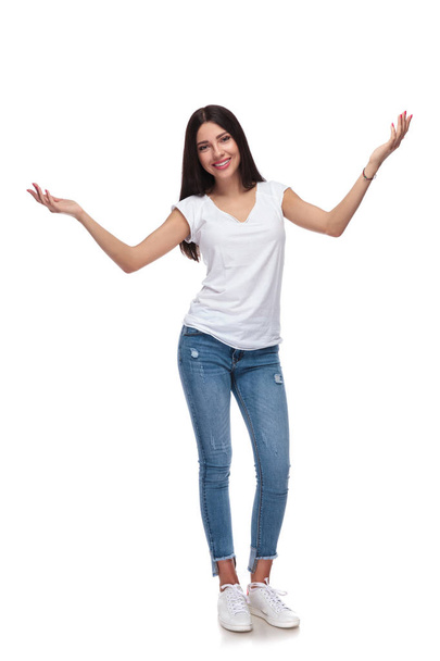 casual μελαχρινή γυναίκα στέκεται πάνω σε λευκό φόντο και την αύξηση της χέρια, πλήρη εικόνα σώματος - Φωτογραφία, εικόνα