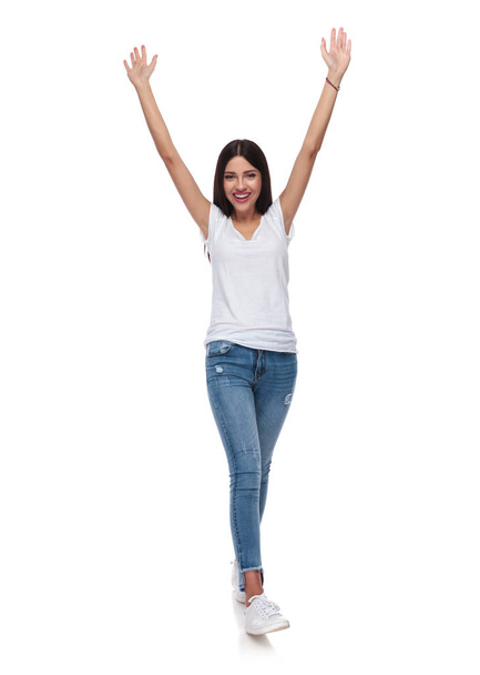 beautiful brunette woman in white t-shirt stepping and celebrating on white background with hands in the air, full length picture - Фото, зображення