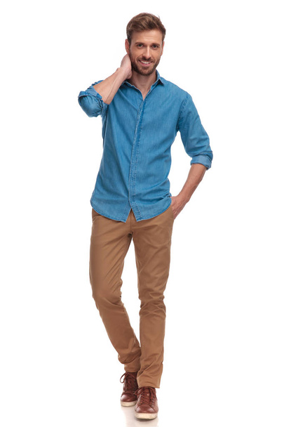young casual man standing and posing on white background, with one hand in pochet and one behind his head - Photo, Image