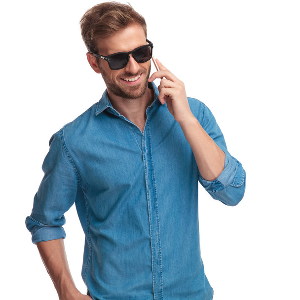 laughing young man wearing sunglasses talks on the phone on white background - Фото, изображение