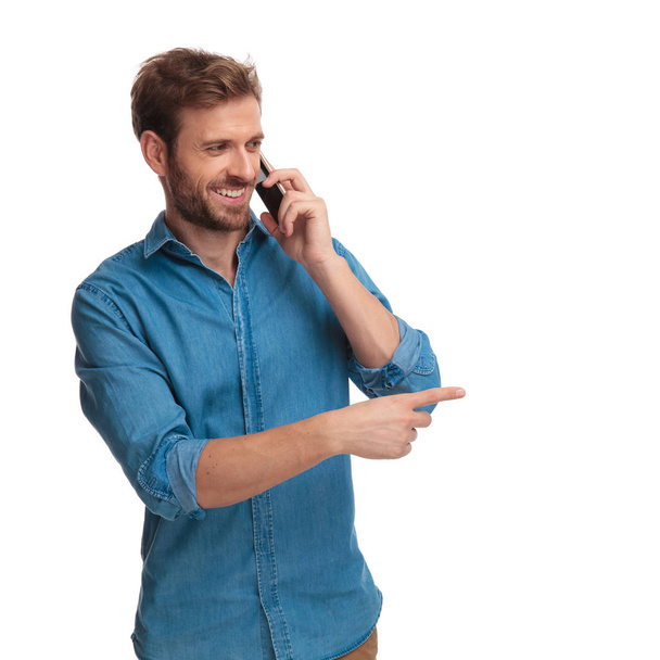 何か白い背景の上で側に電話ポイントの指に話しているカジュアルな男性の笑顔 - 写真・画像