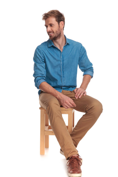 hombre casual sentado en silla de madera se ve a un lado sobre fondo blanco
 - Foto, Imagen