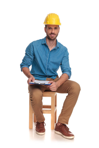 junger sitzender Bauingenieur mit Klemmbrett, auf weißem Hintergrund - Foto, Bild