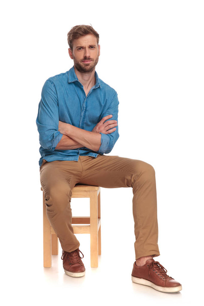 vážný mladý příležitostné muž sedí s rukama na bílém pozadí - Fotografie, Obrázek