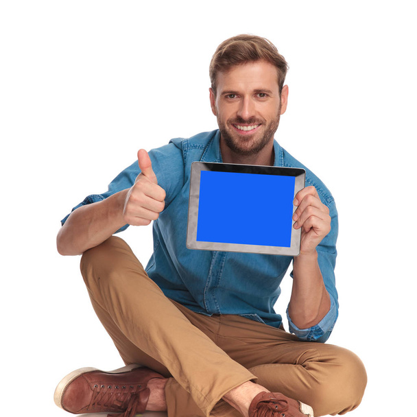sentado hombre casual que muestra la pantalla de la tableta y hace signo ok sobre fondo blanco
 - Foto, imagen