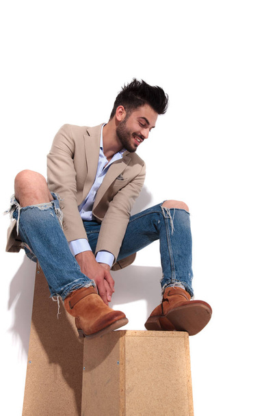 χαμογελώντας περιστασιακή άνθρωπος σε καφέ κοστούμι στηρίζεται σε ξύλινα κιβώτια και κοιτάζοντας προς τα κάτω πλευρά σε λευκό φόντο - Φωτογραφία, εικόνα