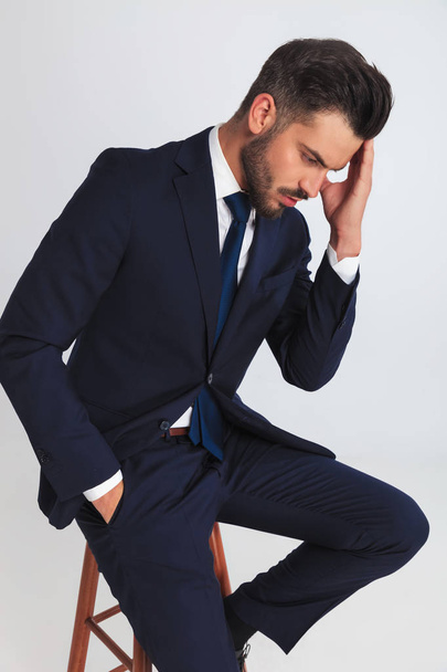 giovane uomo d'affari premuroso che indossa un abito della marina sta guardando da una parte mentre seduto su una sedia di legno, ritratto
 - Foto, immagini