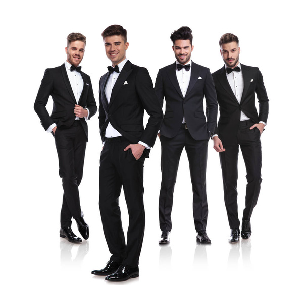 czterech mężczyzn elegancka w tuxedoes stojąc na białym tle z rękami w kieszeniach, obraz pełnej długości - Zdjęcie, obraz