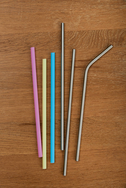 herbruikbare RVS rietjes en wegwerp kleur rietjes op een houten tafel - Foto, afbeelding