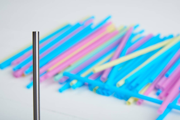 Крупный план многоразовой соломы из нержавеющей стали на фоне одноразовых цветных соломинок на деревянном столе
 - Фото, изображение