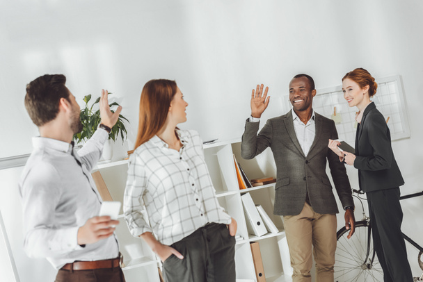 empresários multiculturais sorridentes acenando as mãos no escritório
 - Foto, Imagem