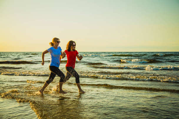 Teenage girl and woman jogging together by seashore - Photo, image