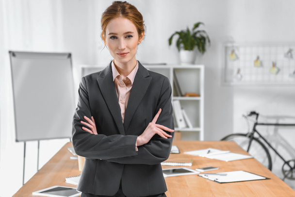 businesswoman with arms crossed looking at camera at office space  - Zdjęcie, obraz