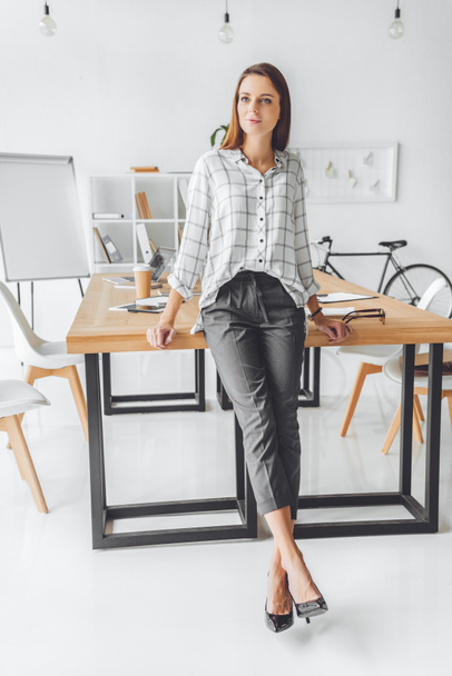 woman in shirt leaning on table and looking away at office space  - Foto, Bild