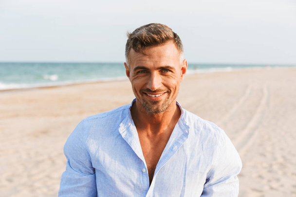 Retrato de un hombre guapo sonriente con camisa de pie en la playa
 - Foto, Imagen