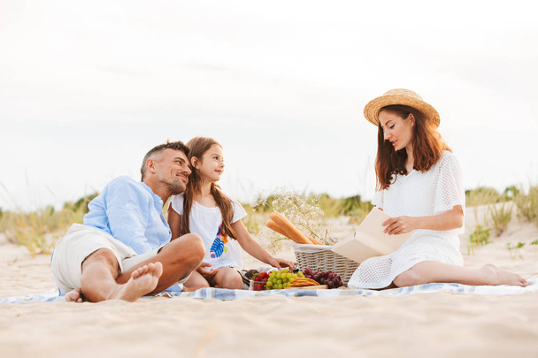 Lovely family with father, mother, daughter having picnic at the beach - Photo, Image