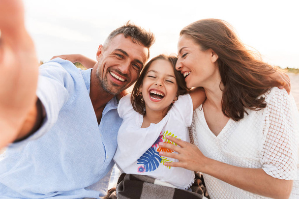 Image of young happy family outdoors at the beach take a selfie by camera. - Foto, immagini