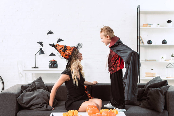 little boy in vampire costume screaming at mother in witch halloween costume at home - Foto, Imagen