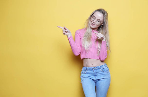 lifestyle and people concept - Portrait of a pretty blond girl pointing finger away over yellow background - Photo, Image