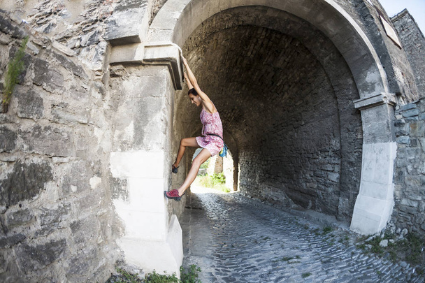 Una mujer en un vestido está escalando una pared de ladrillo. La chica se sube a una valla de piedra. Escalador en una calle de la ciudad. La pared del viejo edificio destruido. Lente de ojo de pez
. - Foto, Imagen