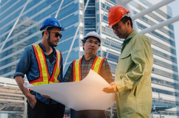 group of engineer, technician and architect with safety helmet planning about building plan with blueprint in modern city building background, construction site, business, industry and worker concept - Foto, Imagen