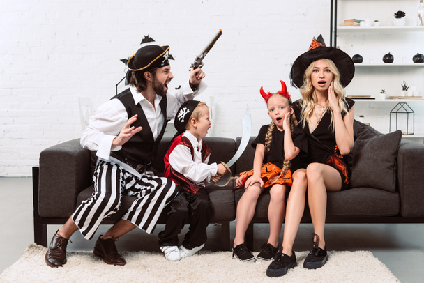 Vater und Sohn in Piratenkostümen erschrecken Mutter und Tochter auf dem heimischen Sofa - Foto, Bild