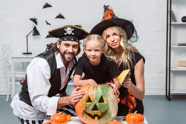 portrait of parents and little daughter in halloween costumes at table with pumpkins at home - Photo, Image