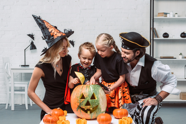 family in various halloween costumes at table with pumpkins in kitchen at home - Photo, Image