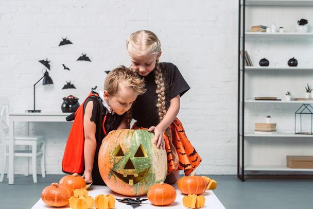 Маленькие дети в костюмах на Хэллоуин смотрят в тыкву дома
 - Фото, изображение