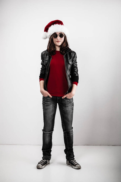 Metalhead girl in santa hat and sunglasses posing on grey background - Photo, image