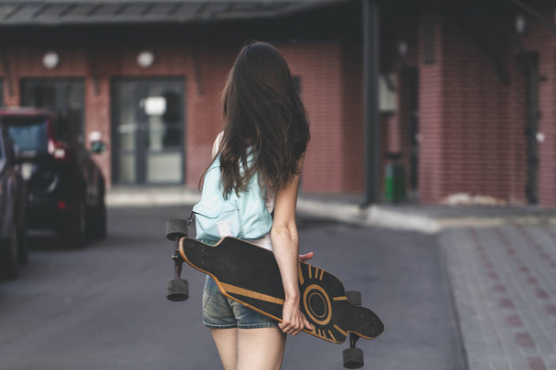 girl with long hair holding long board on city street - Foto, afbeelding
