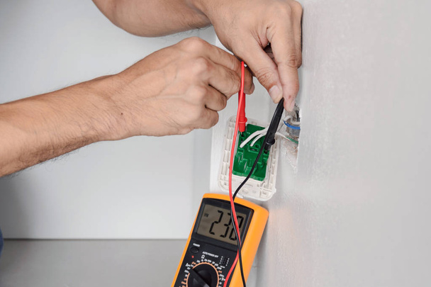 Electrician is using a digital meter to measure the voltage at the power outlet in on the wall. - Foto, afbeelding