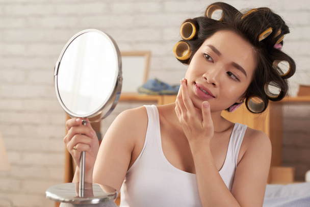 Jolie jeune femme asiatique avec des bigoudis de cheveux regardant miroir
 - Photo, image